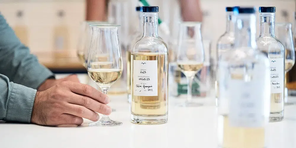 Glass of Maison Lineti single malt and bottle on a textured surface.